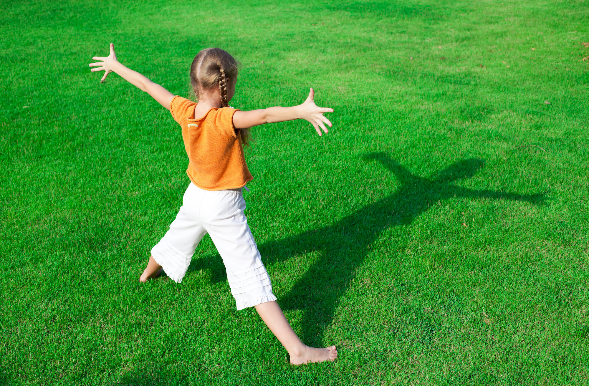 a girl standing on the grass  looking at his shadow